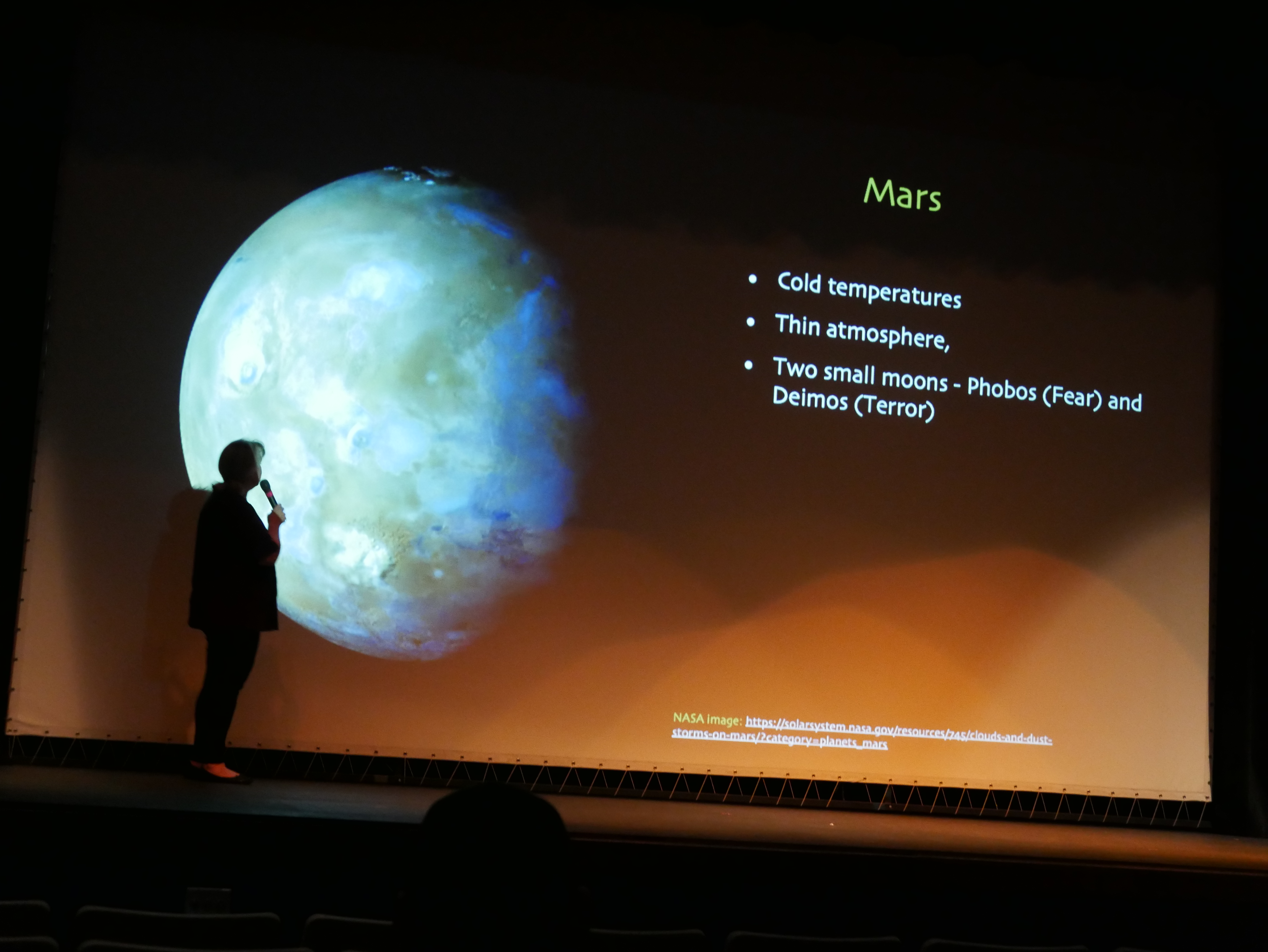 The silhouette of a woman speaker in front of an image of Mars against a dark background, with the words 